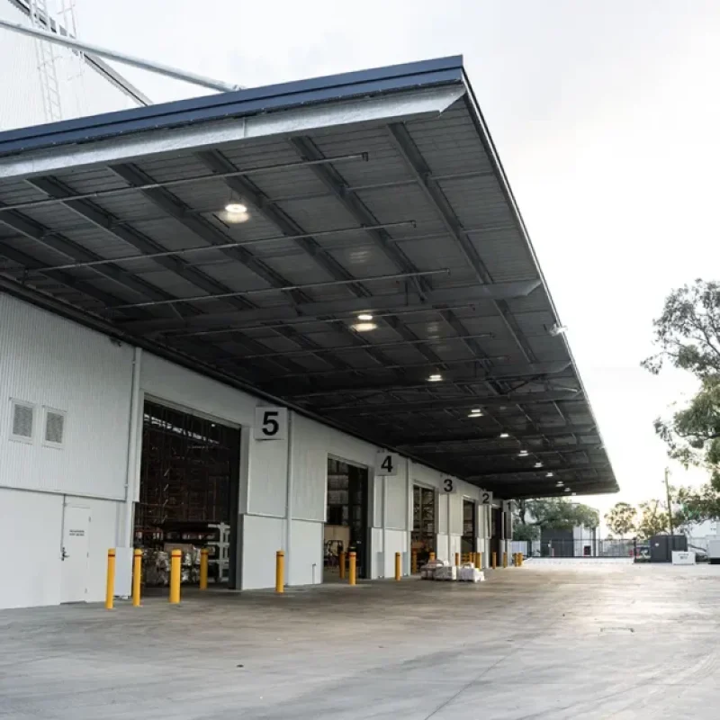 Industrial warehouse loading dock with multiple roller shutter bays, overhead canopy lighting and a concrete loading area.
